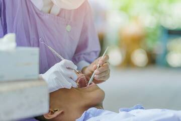 Female dentist examining teeth of a student with mouth mirror and probe checking in school.