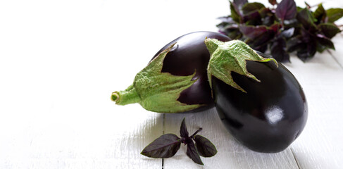 Fresh eggplants and aromatic herbs on a white wooden background.