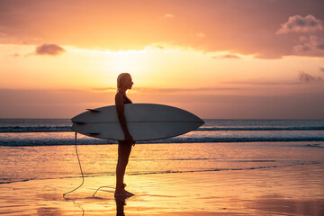 Fototapeta na wymiar Portrait of surfer girl with beautiful body on the beach with surfboard at colourful sunset time