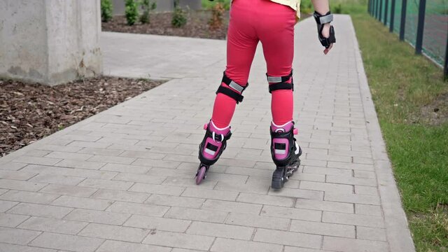 A 5-6 year old girl is rollerblading in the courtyard of an apartment building. The child is just beginning to master roller skates, so he often falls.