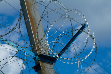 Rusty Metal Construction with Barbed Wire against a Blue Sky with light light clouds. Background image symbolizing the restriction of freedom and the opposition of brute strength and fragile nature