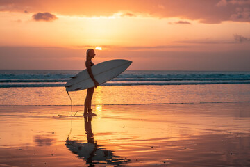 Portrait of surfer girl with beautiful body on the beach with surfboard at colourful sunset time.