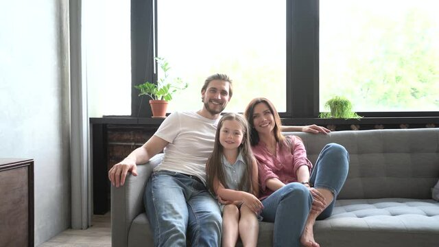 Happy family portrait, young adult foster parents mother and father bonding with funny cute children kids laughing look at camera posing together on couch in modern home