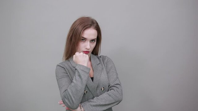 Angry and aggressive, shaking fist in a threatening way, domestic violence. Young attractive woman, dressed gray jacket, with green eyes, light brown hair, background
