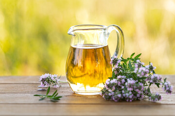 Thyme essential oil in a glass jug and branches of a fresh thyme plant with flowers on a wooden background. Copy space