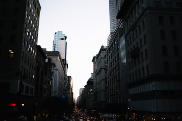 Dark urban architecture in evening on street with busy traffics and jams in business center of city , tall buildings and skyscraper in downtown with black exterior of commercial real estate .