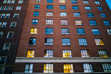 Exterior of brown brick tall building and lights in windows of residential flats and apartments in town, high vintage facade of rental loft real estate for commercial property in megalopolis