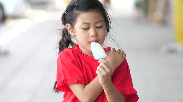 Asian girl eating ice cream popsicle outdoors