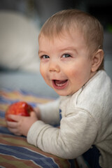 Fototapeta na wymiar Bebé jugando, riendo y comiendo una manzana mirando hacia la cámara