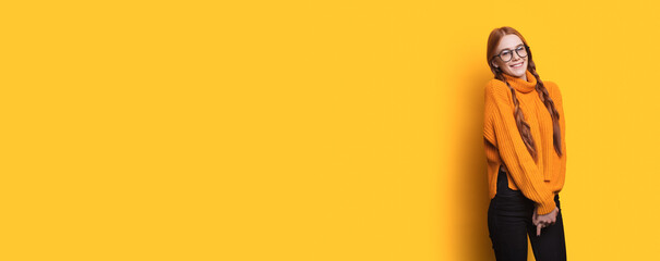 Sweet caucasian woman with red hair and freckles wearing eyeglasses posing on a yellow wall with free space