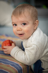 Bebé jugando, haciendo una mueca y comiendo una manzana mirando hacia la cámara