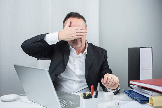 Manager cinquantenne vestito in camicia e giacca nera &egrave; seduto nella sua postazione di lavoro si arrabbia furiosamente conto il proprio computer portatile