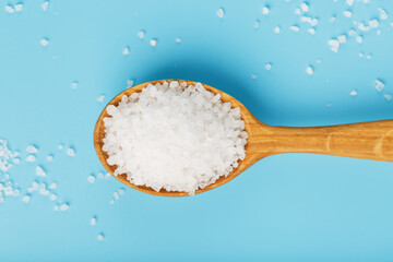 Sea salt in a wooden spoon on a blue background, with scattered salt.
