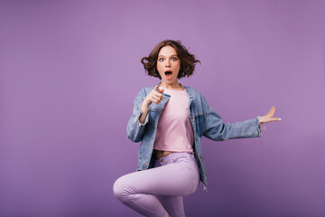 Shocked brown-eyes woman jumping on purple background. Joyful short-haired girl in jacket dancing.