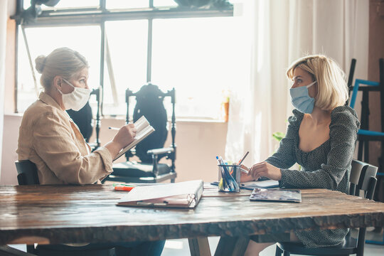 Senior caucasian woman working with a client at home with some documents wearing a medical mask on face