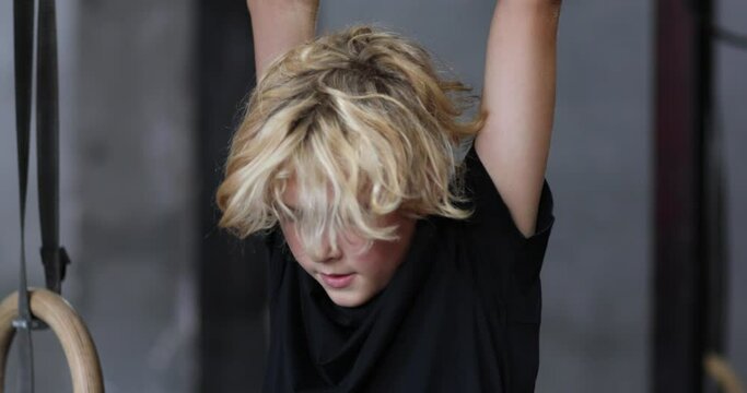 Portrait of cute blond teen boy in black shirt and red shorts pressing at the horizontal bar. 4k video.