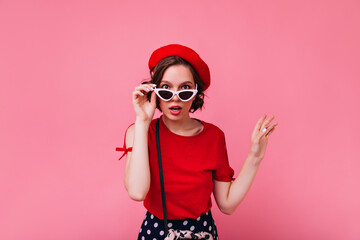 Interested white girl with short hair looking to camera through glasses. Studio photo of magnificent french woman in red outfit.