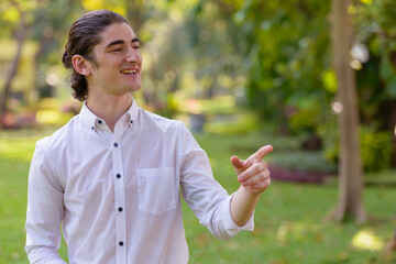 Happy young handsome businessman thinking and pointing finger at the park outdoors