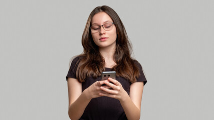 Online chat. Mobile app. Curious woman reading message on phone isolated on gray copy space. Skeptic lady thinking on special offer on Internet.