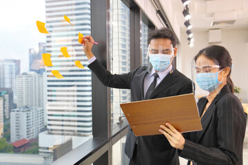 Asian business people making note of new idea for planning strategy following social distancing and new normal policy by wearing facial mask in the business office workplace during covid-19