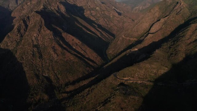 Aerial tilting up shot of steep rugged mountains cast in shadow. 4K