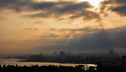 Fototapeta premium Sunset landscape on the city coast. Clouds and sun rays over the buildings.