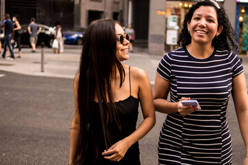 Young women walking around a square in the city while using their electronic devices