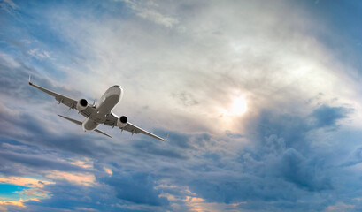 Fototapeta na wymiar White passenger airplane in the sunset clouds - Travel by air transport