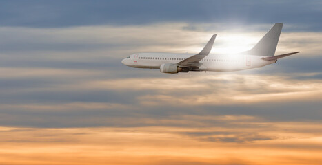 Naklejka na ściany i meble White passenger airplane in the sunset clouds - Travel by air transport