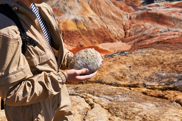 paleontologist holding a dinosaur egg in his hands on the background of the desert, close-up