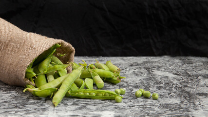 green peas, pods and peas in a canvas bag on a concrete background, a woman peels