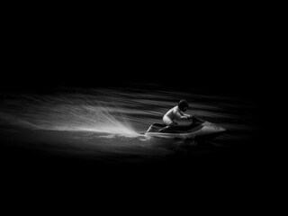 RC controlled jet ski model on lake on black background.