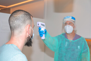 Healthcare worker measuring customer temperature with contactless thermometer