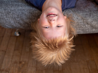 handsome blond boy plays on couch, lifts his head and pulls his gorgeous hair down.