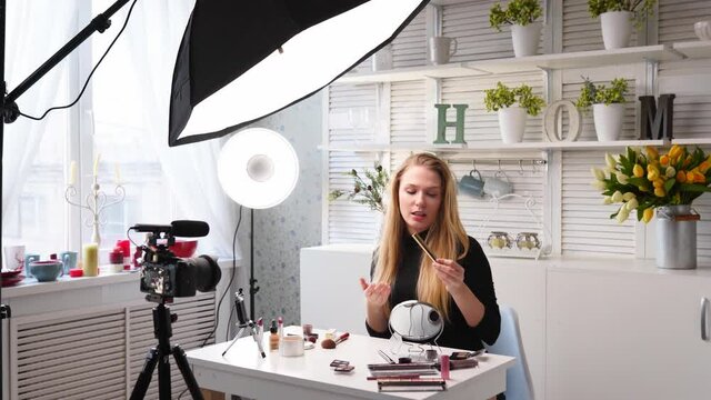 Beauty blogger woman filming daily make-up routine tutorial on camera. Influencer blonde girl live streaming eyelashes mascasra review in home studio with professional lighting equipment. Vlogger job.