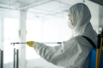 A man wearing disinfection suit spraying with sanitizer the glass doors' handles in an empty...