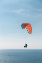 A paraglider flies over the sea in the blue sky on a sunny summer day. Bright blue sea, summer, freedom, adventure, relaxation