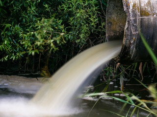 Long exposure shot of a concrete pipe transporting the polluted sewage water in to a small pond.