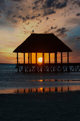 Pier over Caribbean Ocean at sunset, a little bird in the top of the hut, reflections on the water of the Caribbean Sea, Holbox, Mexico