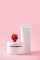 Cosmetic still life. Containers and a strawberry on a pink background. Minimalistic composition. Blank label for branding