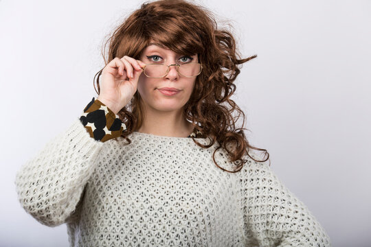 Signora con capelli mossi castani e maglione sguarda con espressione molto severa e meravigliata toccandosi gli occhiali, isolata su sfondo bianco 