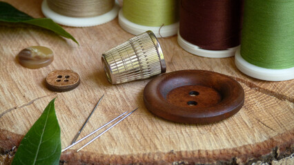 Fototapeta na wymiar Rustic Sewing Equipment | Sewing Needles with Thimble and Buttons Surrounded by Spools of Thread