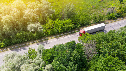 Truck logistic aerial. Wagon driving by the roadway between green forest.