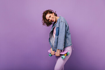 Enthusiastic short-haired woman in denim jacket holding longboard. Winsome white girl with trendy...