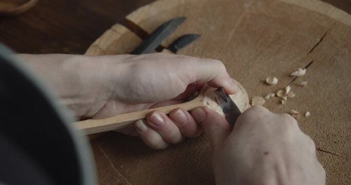 Woman carpenter carves piece of wood making a spoon close-up