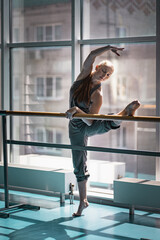 Young woman doing stretching on ballet barre.