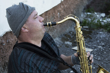 A homeless street musician sits on the street with a saxophone to earn food.