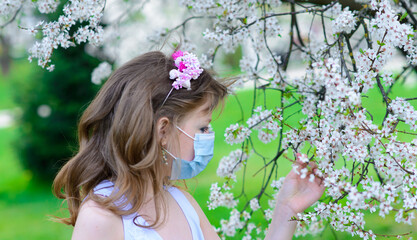 Lonely teenage girl wearing protection medicine mask against virus and allergy enjoying spring flower blossom in blooming garden