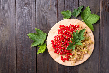 White and red currants with leaves on a round board on a wooden table.