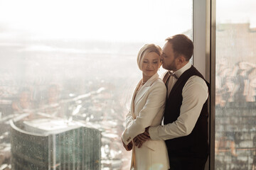 Wedding couple standing by the window of skyscraper.